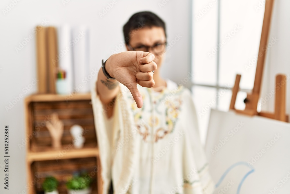 Young hispanic woman with short hair at art studio looking unhappy and angry showing rejection and negative with thumbs down gesture. bad expression. Young hispanic woman with short hair at art studio looking unhappy and angry showing rejection and negative with thumbs down gesture. bad expression.