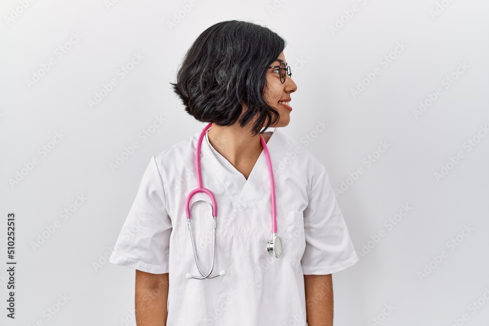 Young hispanic doctor woman wearing stethoscope over isolated background looking to side, relax profile pose with natural face with confident smile. Young hispanic doctor woman wearing stethoscope over isolated background looking to side, relax profile pose with natural face with confident smile.