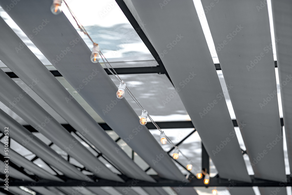 Φωτογραφία Decorative white textile strips of fabric on roof of awning for sun protection of gazebo on terrace of backyard with strip of line garland with bulbs, a close-up of ceiling decor