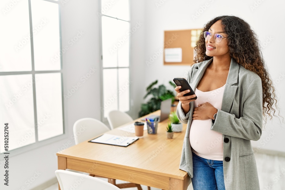 Young latin woman pregnant smiling confident using smartphone working at office