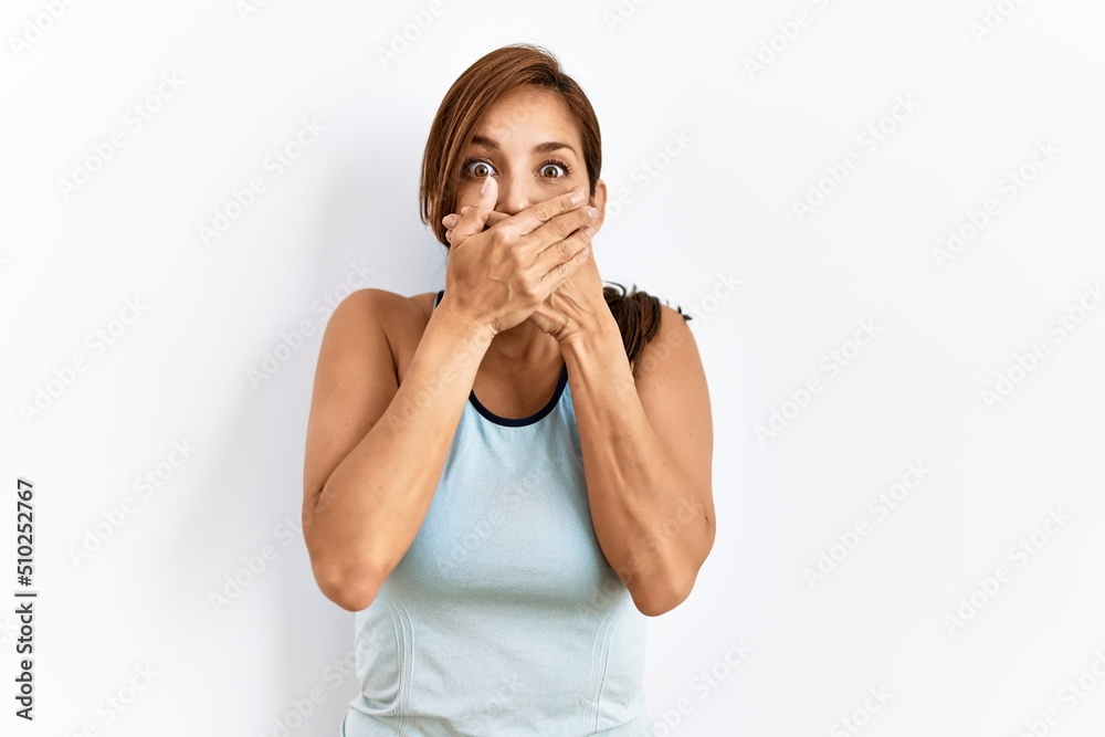 Young latin woman wearing sporty clothes over isolated background shocked covering mouth with hands for mistake. secret concept. Young latin woman wearing sporty clothes over isolated background shocked covering mouth with hands for mistake. secret concept.