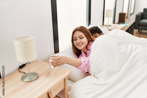 Young couple slepping on the bed at bedroom. Woman drinking glass of water.