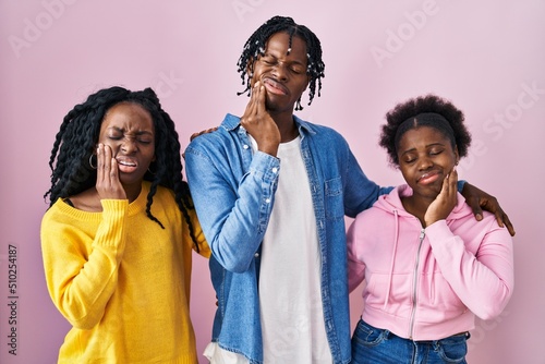 Group of three young black people standing together over pink background touching mouth with hand with painful expression because of toothache or dental illness on teeth. dentist concept.