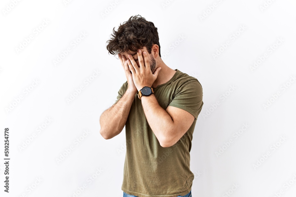 Hispanic man standing over isolated white background with sad expression covering face with hands while crying. depression concept. Hispanic man standing over isolated white background with sad expression covering face with hands while crying. depression concept.