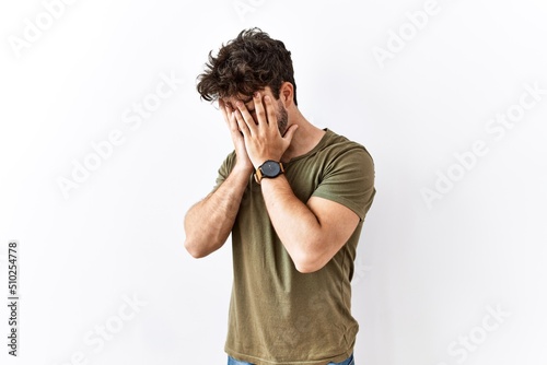 Hispanic man standing over isolated white background with sad expression covering face with hands while crying. depression concept.