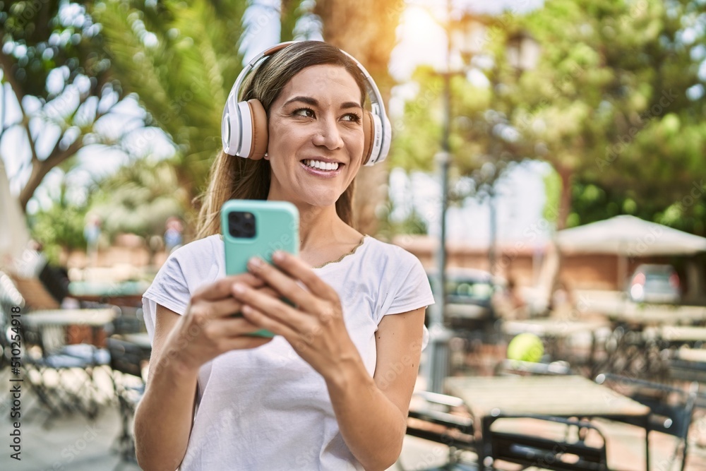 Young hispanic woman smiling confident using smartphone and headphones at park