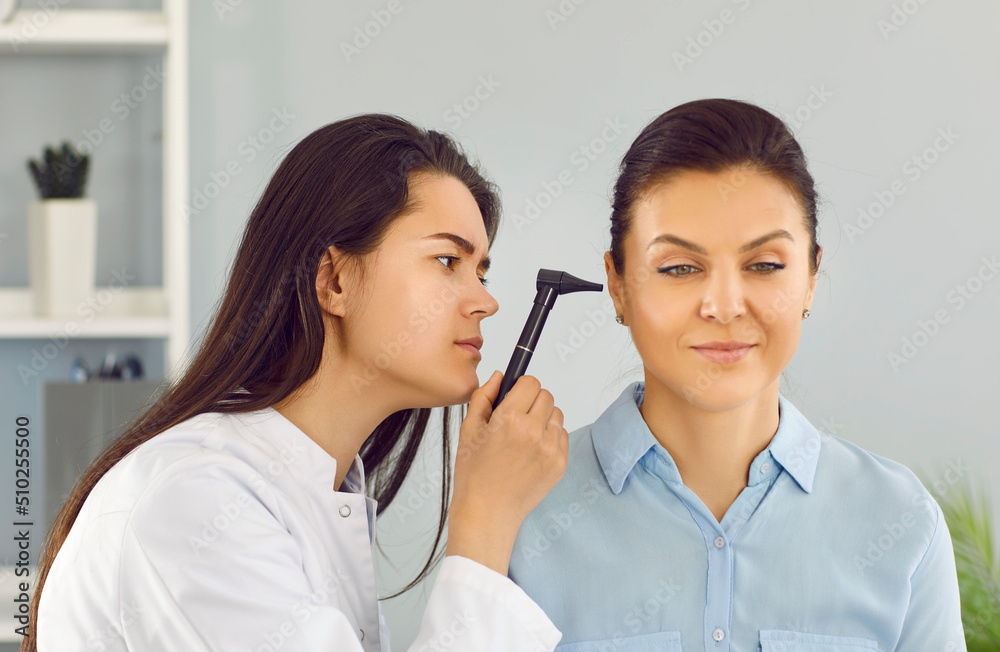 ENT doctor aka otolaryngologist holding otoscope and examining patient's ear. Beautiful young woman gets ear examination and receives professional correct therapy prescription. Medical checkup concept ENT doctor aka otolaryngologist holding otoscope and examining patient's ear. Beautiful young woman gets ear examination and receives professional correct therapy prescription. Medical checkup concept