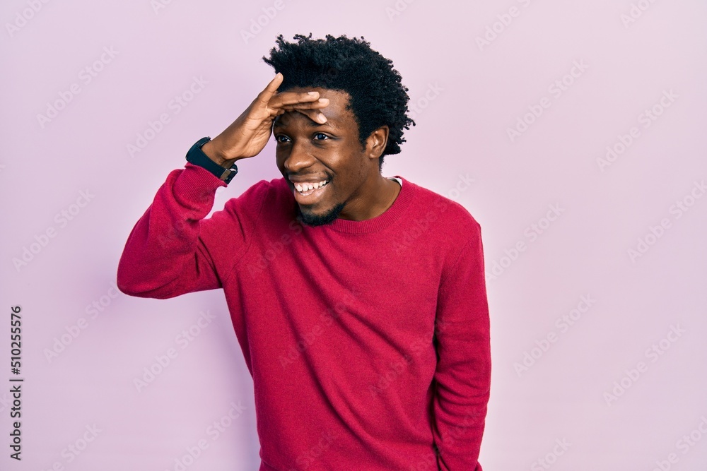 Young african american man wearing casual clothes very happy and smiling looking far away with hand over head. searching concept. Young african american man wearing casual clothes very happy and smiling looking far away with hand over head. searching concept.