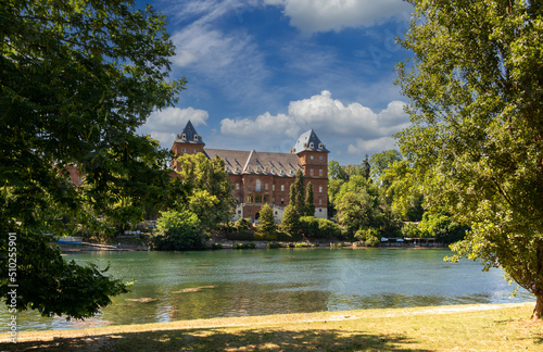 Turin, Piedmont, Italy: the river Po with the Valentino castle (Castello del Valentino) among the trees in the park on the river and with blue sky and white clouds
