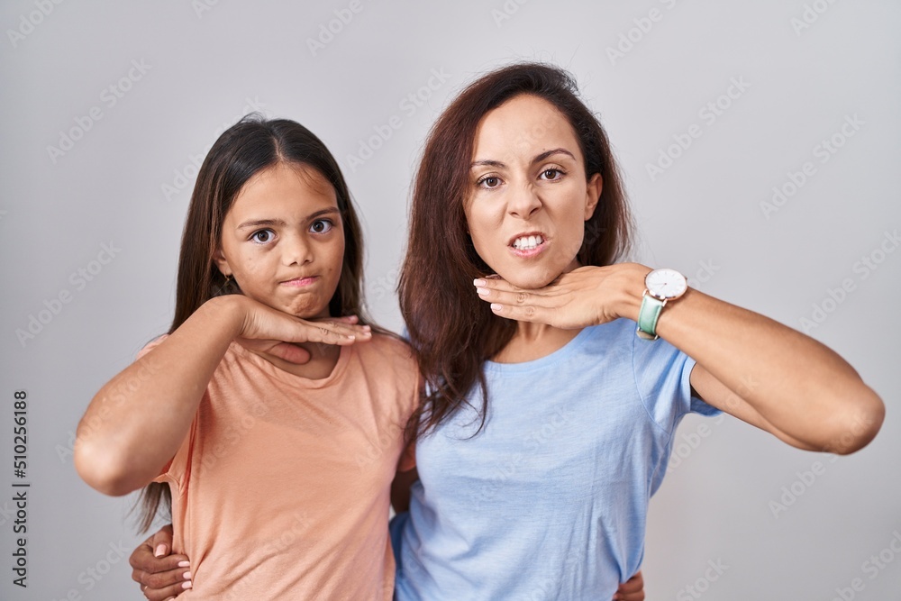 Young mother and daughter standing over white background cutting throat with hand as knife, threaten aggression with furious violence Young mother and daughter standing over white background cutting throat with hand as knife, threaten aggression with furious violence