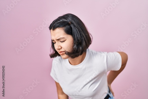 Young hispanic woman wearing casual white t shirt over pink background suffering of backache, touching back with hand, muscular pain
