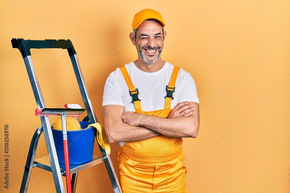 Handsome middle age man with grey hair window cleaner crossing arms winking looking at the camera with sexy expression, cheerful and happy face. Handsome middle age man with grey hair window cleaner crossing arms winking looking at the camera with sexy expression, cheerful and happy face.