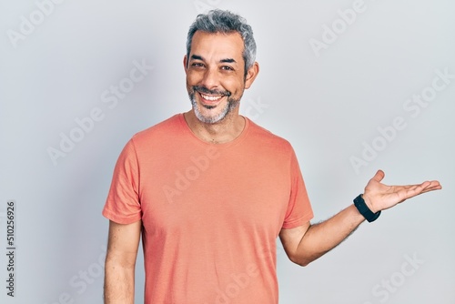 Handsome middle age man with grey hair wearing casual t shirt smiling cheerful presenting and pointing with palm of hand looking at the camera.