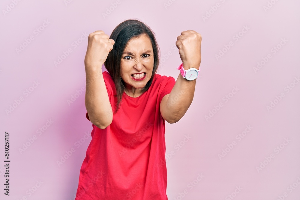 Middle age hispanic woman wearing casual clothes angry and mad raising fists frustrated and furious while shouting with anger. rage and aggressive concept.
