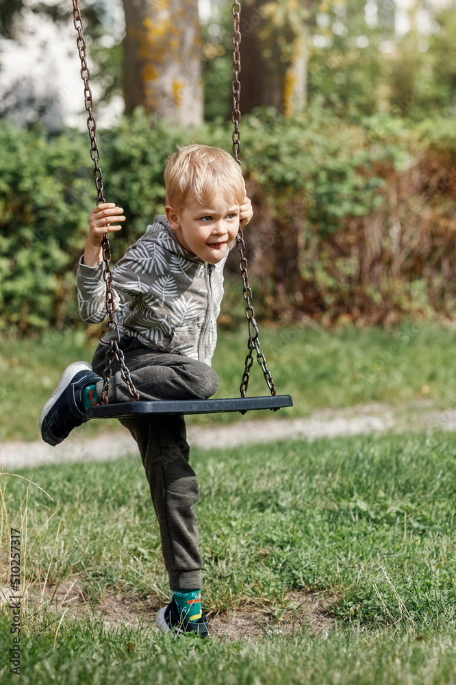 The blond boy plays with a chain swing as he tries to climb on it without his parents help.