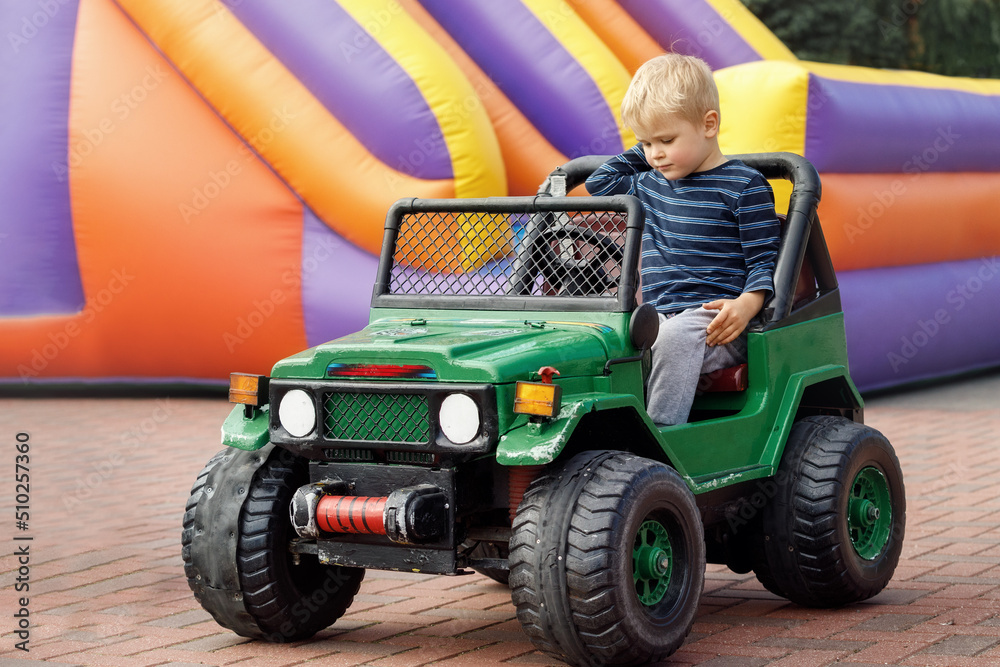Little child driving green toy car, colored inflatable trampoline in background