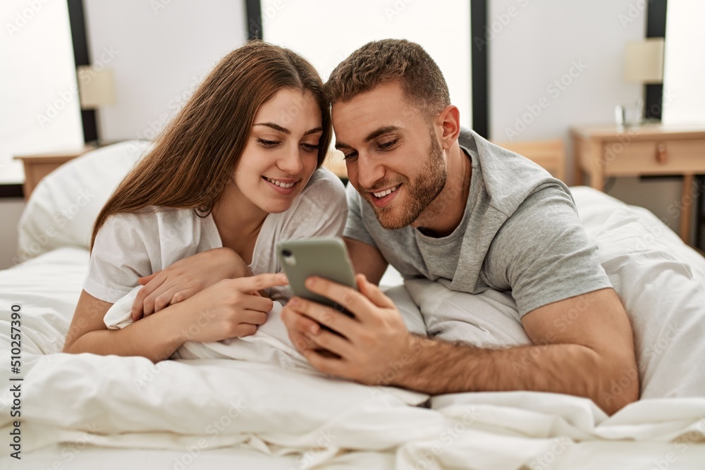 Young caucasian couple using smartphone lying on bed at home. Young caucasian couple using smartphone lying on bed at home.