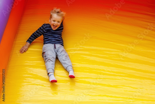A hilarious little boy slides down at a high speed off a large, bright yellow trampoline. Child on the move, there is free space for text in the photo