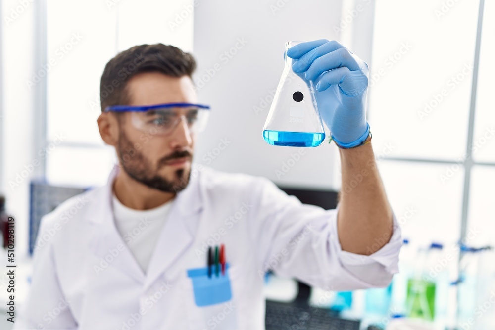 Young hispanic man wearing scientist uniform holding test tube at laboratory Young hispanic man wearing scientist uniform holding test tube at laboratory
