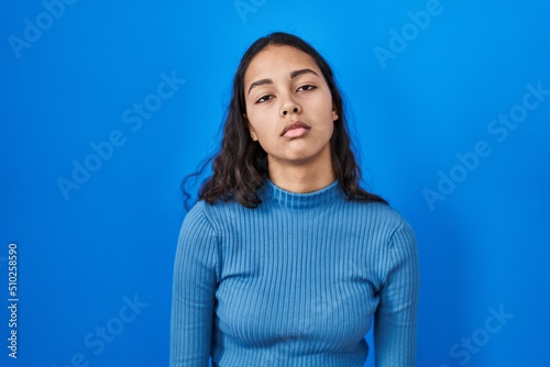 Young brazilian woman standing over blue isolated background looking sleepy and tired, exhausted for fatigue and hangover, lazy eyes in the morning.