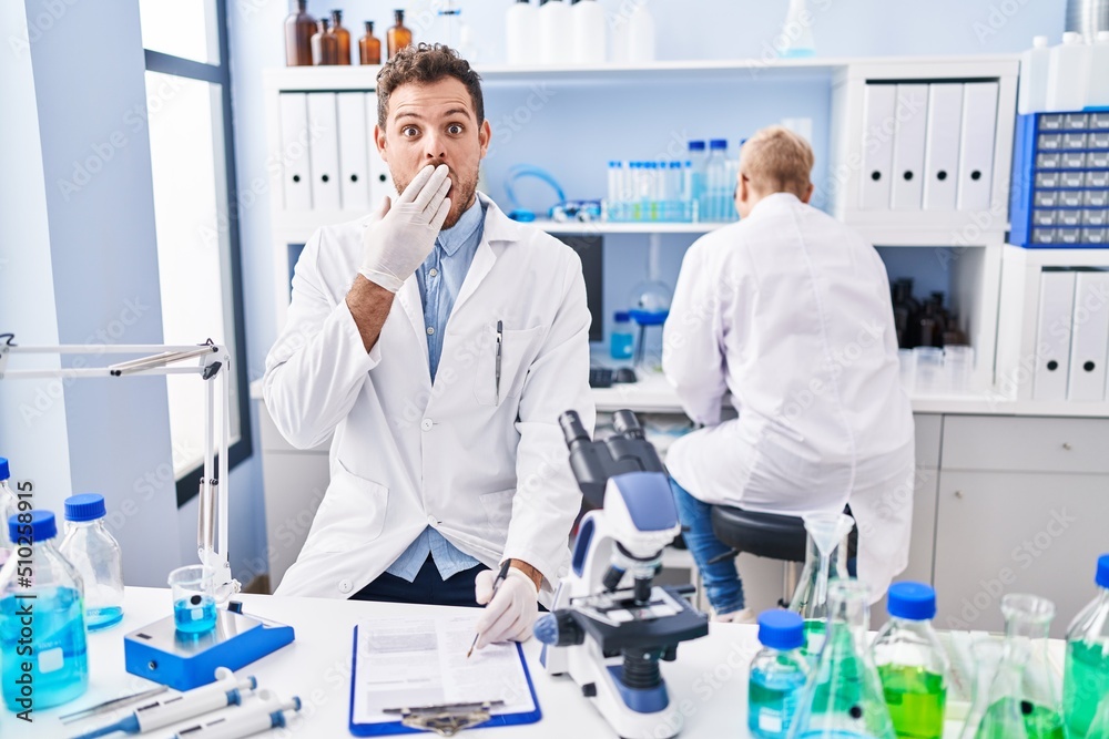 Hispanic man and woman working at scientist laboratory covering mouth with hand, shocked and afraid for mistake. surprised expression Hispanic man and woman working at scientist laboratory covering mouth with hand, shocked and afraid for mistake. surprised expression