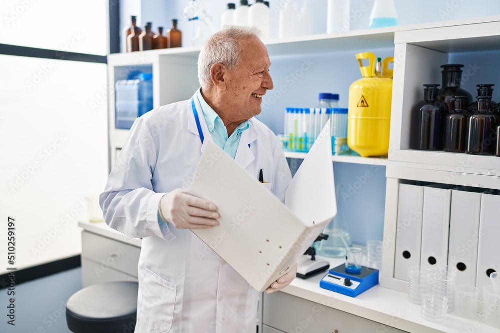 Senior man wearing scientist uniform reading document at laboratory Senior man wearing scientist uniform reading document at laboratory