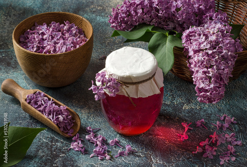 Healthy lilac flowers syrup in glass jar and lilac flower petals on textured background.