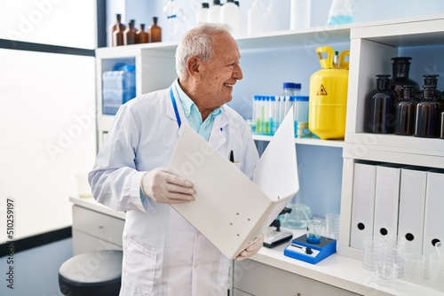 Senior man wearing scientist uniform reading document at laboratory