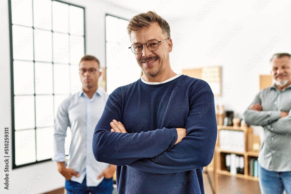 Middle age businessman smiling with arms crossed gesture standing with work partners at the office. Middle age businessman smiling with arms crossed gesture standing with work partners at the office.