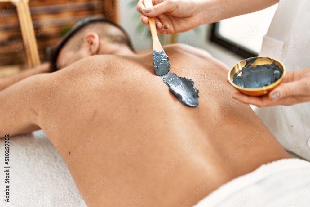 Fototapeta premium Young hispanic man relaxed having skin back treatment at beauty center