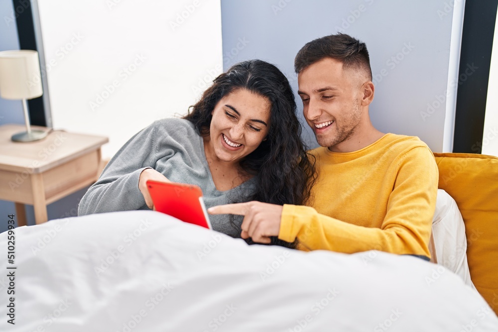 Man and woman couple watching video on touchpad sitting on bed at bedroom Man and woman couple watching video on touchpad sitting on bed at bedroom