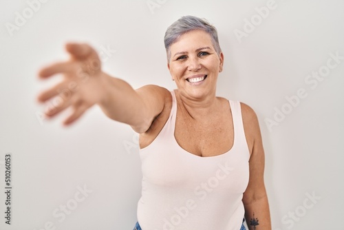 Middle age caucasian woman standing over white background smiling friendly offering handshake as greeting and welcoming. successful business.