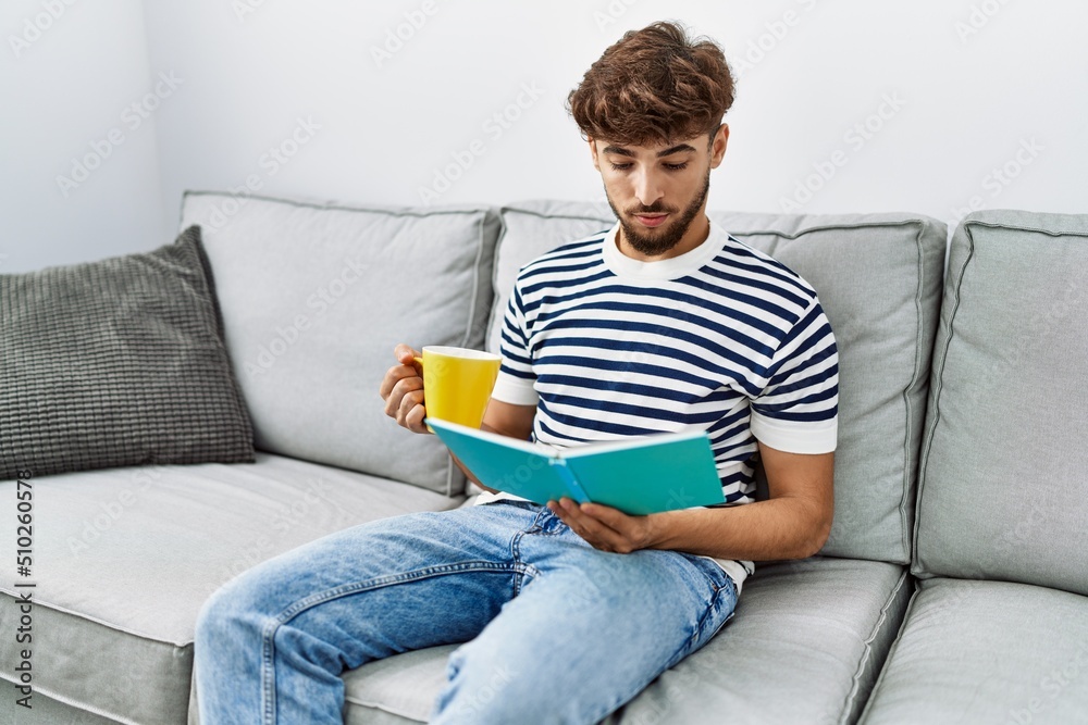 Young arab man reading book drinking coffee at home Young arab man reading book drinking coffee at home