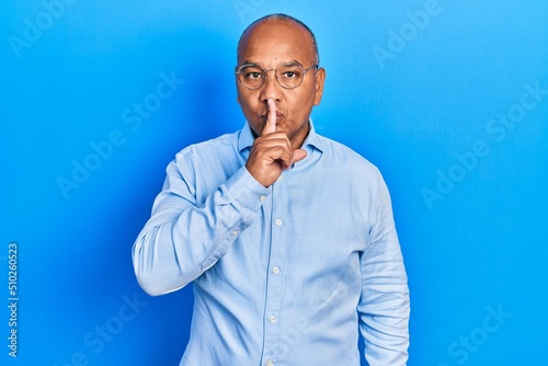 Middle age latin man wearing casual clothes and glasses asking to be quiet with finger on lips. silence and secret concept.