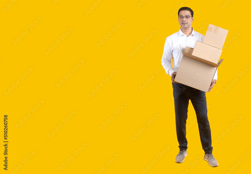 Man with boxes. Guy is engaged in relocation. Indian businessman with glasses on yellow. Young man makes relocation. Human is holding several parcels. Concept of providing relocation services.
