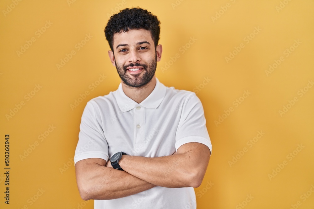 Arab man standing over yellow background happy face smiling with crossed arms looking at the camera. positive person. Arab man standing over yellow background happy face smiling with crossed arms looking at the camera. positive person.