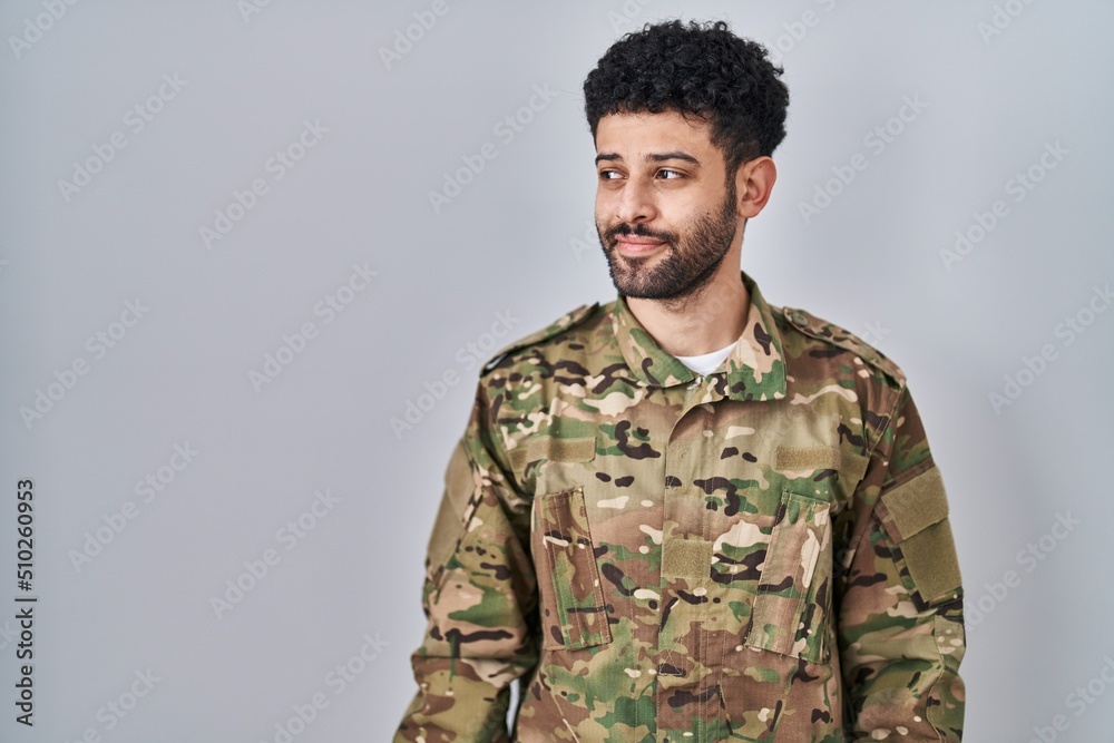 Arab man wearing camouflage army uniform smiling looking to the side and staring away thinking.