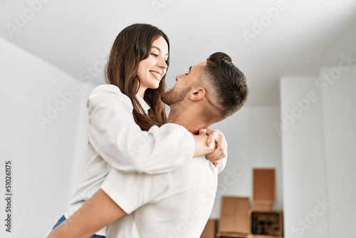 Young hispanic man holding woman in arms and hugging at new home.