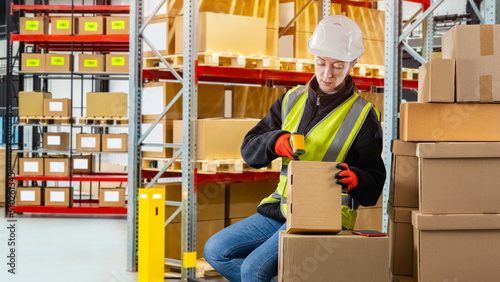 Warehouse worker. Warehouse specialist scans bar code for parcels. Woman warehouse worker in protective hard hat. Employee of modern logistics center. Girl in yellow vest handles parcels