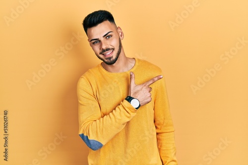 Young hispanic man with beard wearing casual winter sweater smiling cheerful pointing with hand and finger up to the side