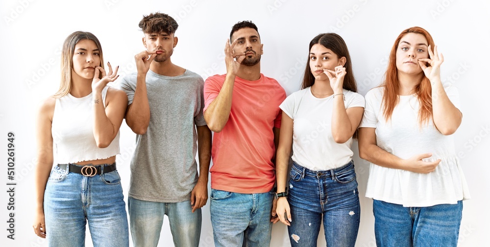 Obraz premium Group of young friends standing together over isolated background mouth and lips shut as zip with fingers. secret and silent, taboo talking