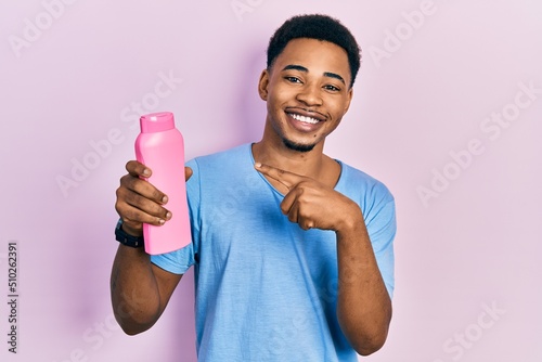 Young african american man holding shampoo bottle smiling happy pointing with hand and finger
