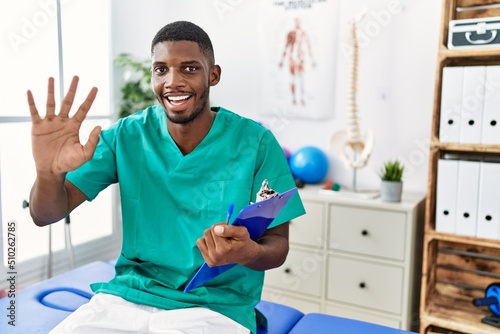 Young african american man working at pain recovery clinic waiving saying hello happy and smiling  friendly welcome gesture