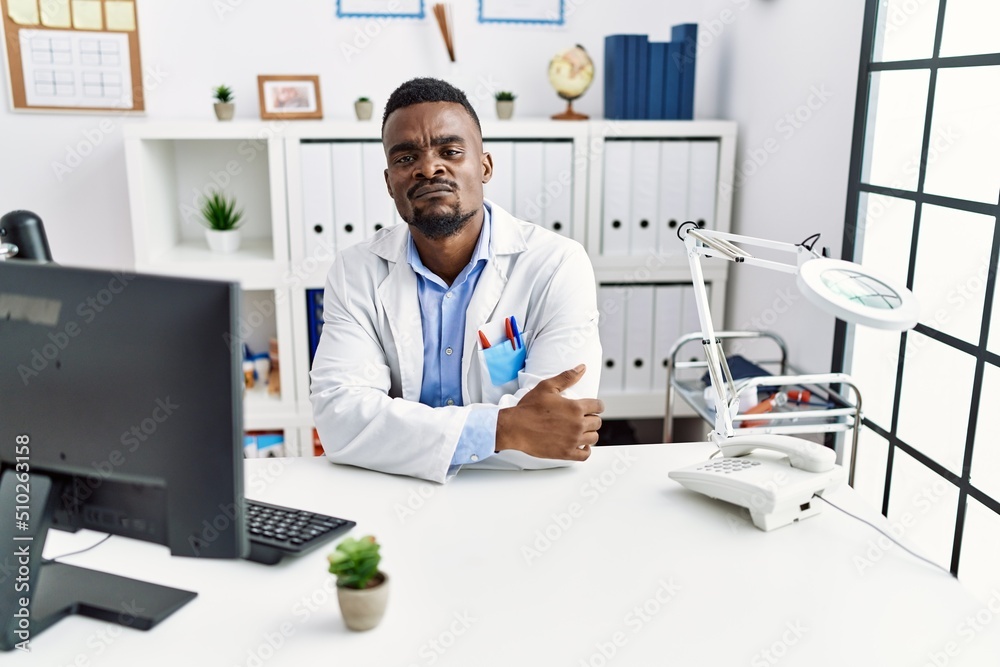 Young african doctor man wearing stethoscope at the clinic skeptic and nervous, disapproving expression on face with crossed arms. negative person.