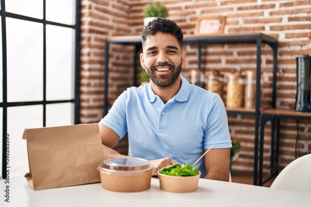 Hispanic man with beard eating delivery salad looking positive and happy standing and smiling with a confident smile showing teeth Hispanic man with beard eating delivery salad looking positive and happy standing and smiling with a confident smile showing teeth
