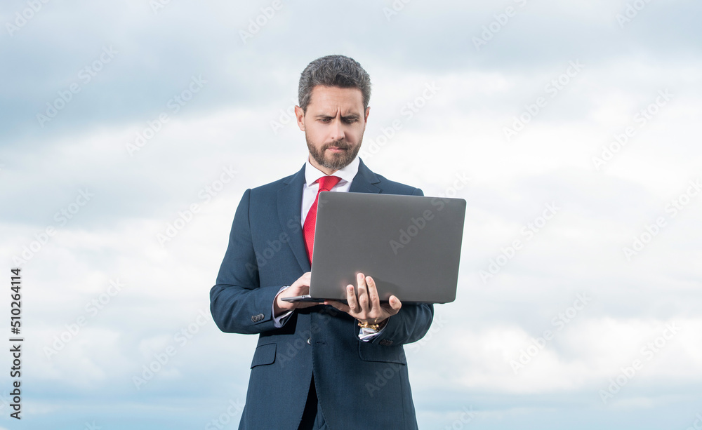 man in suit using laptop on sky background