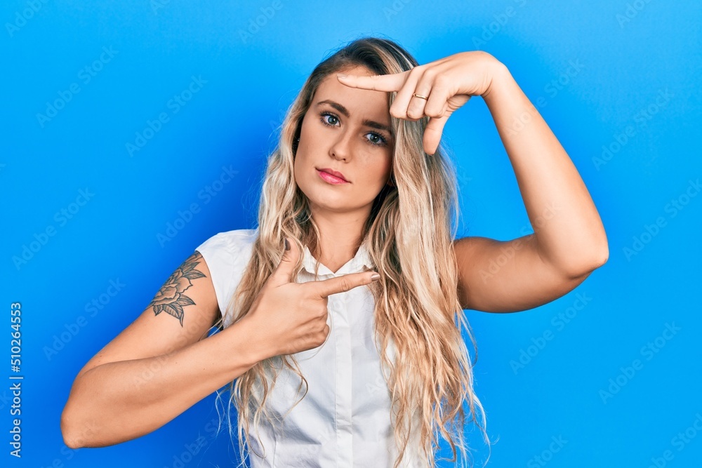 Beautiful young blonde woman doing picture frame gesture with hands relaxed with serious expression on face. simple and natural looking at the camera. Beautiful young blonde woman doing picture frame gesture with hands relaxed with serious expression on face. simple and natural looking at the camera.