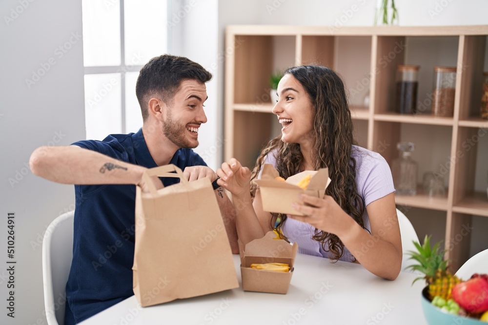 Young hispanic couple eating take away food sitting on table at home Young hispanic couple eating take away food sitting on table at home