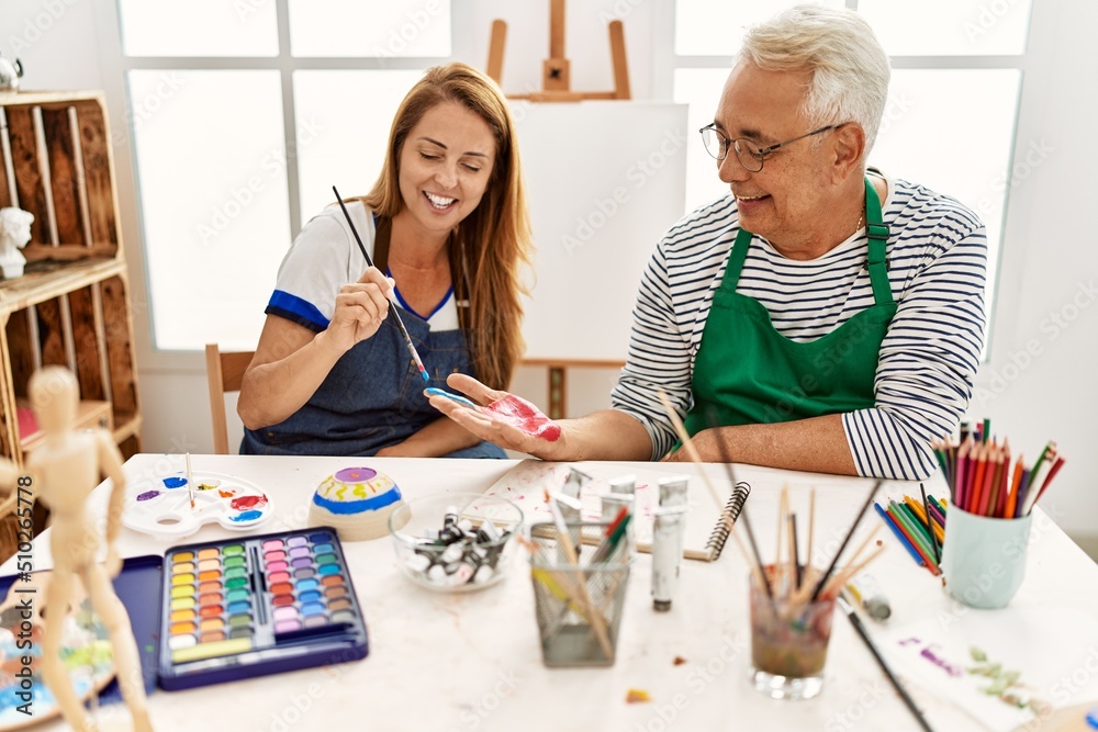 Fototapeta premium Two middle age artists smiling happy painting hands at art studio.
