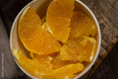Sliced ​​orange served in a clay bowl on rustic wooden table.